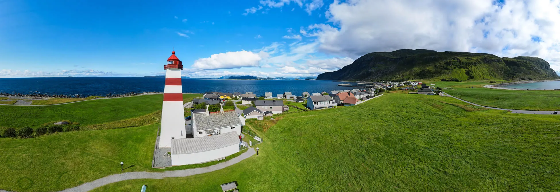 Red and white lighthouse overlooking coastal village and mountains