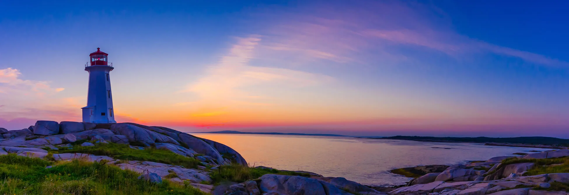 White lighthouse on rocky shore at sunset with colorful sky