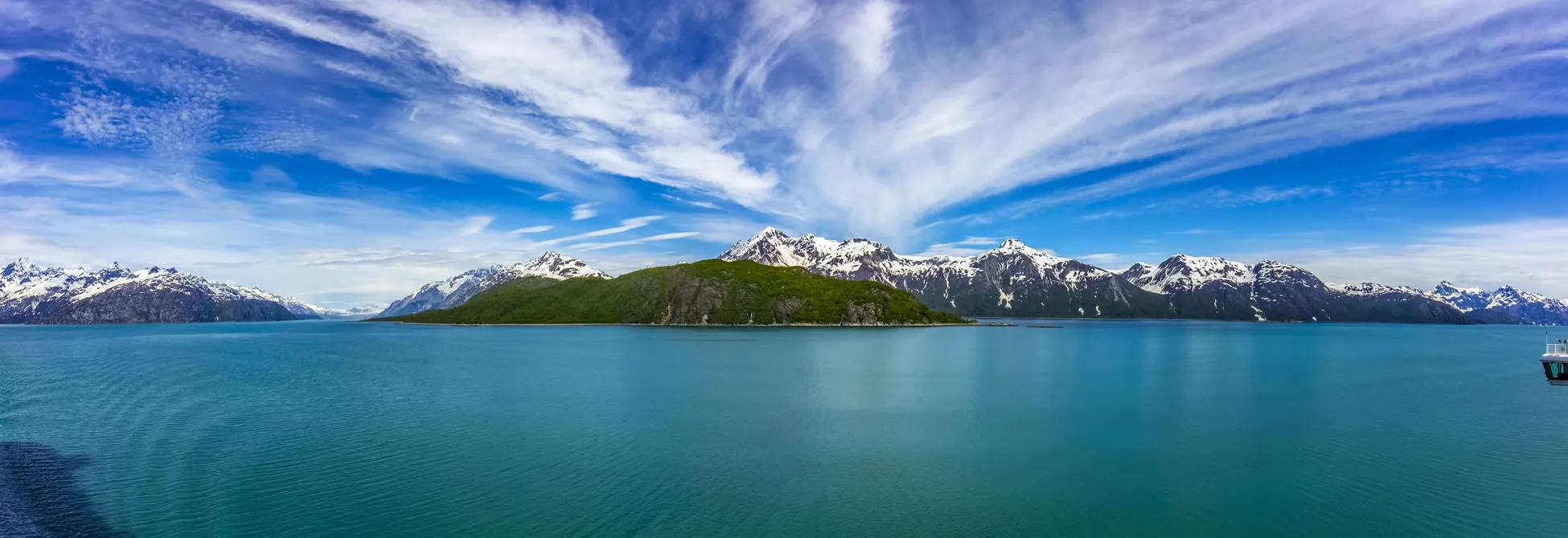 Snow-capped mountains surround turquoise waters of an Alaskan bay