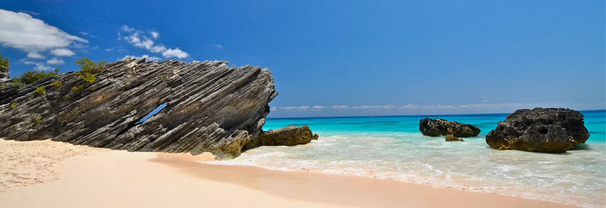 Layered rock formation on pristine beach with turquoise ocean and blue sky