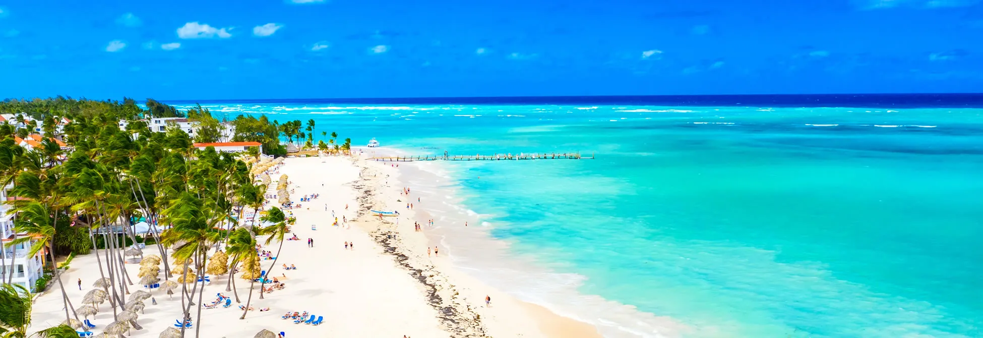 Tropical beach with white sand, turquoise water, palm trees, and sunbathers