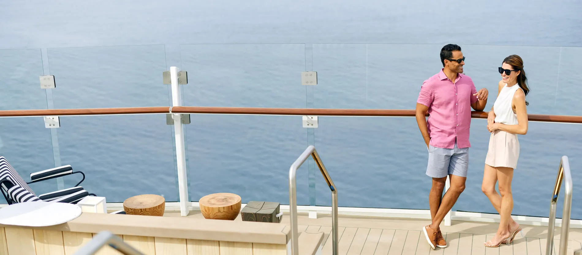 Two people on cruise ship deck with ocean view and wooden furniture