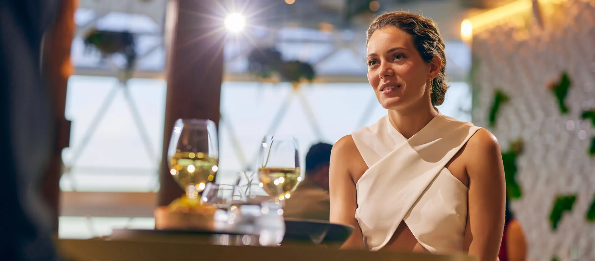 Smiling woman in white top at restaurant with wine glasses in foreground