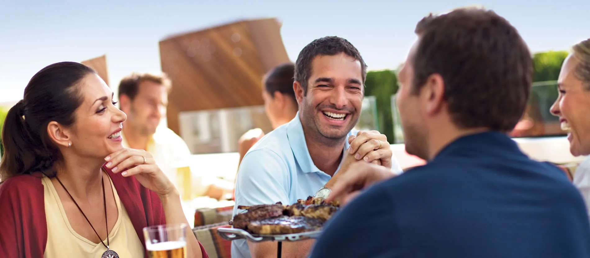Friends laughing and enjoying barbecue meal outdoors on sunny day