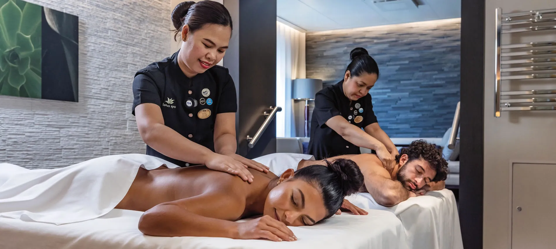 Spa therapists giving massage to two relaxed clients on treatment beds
