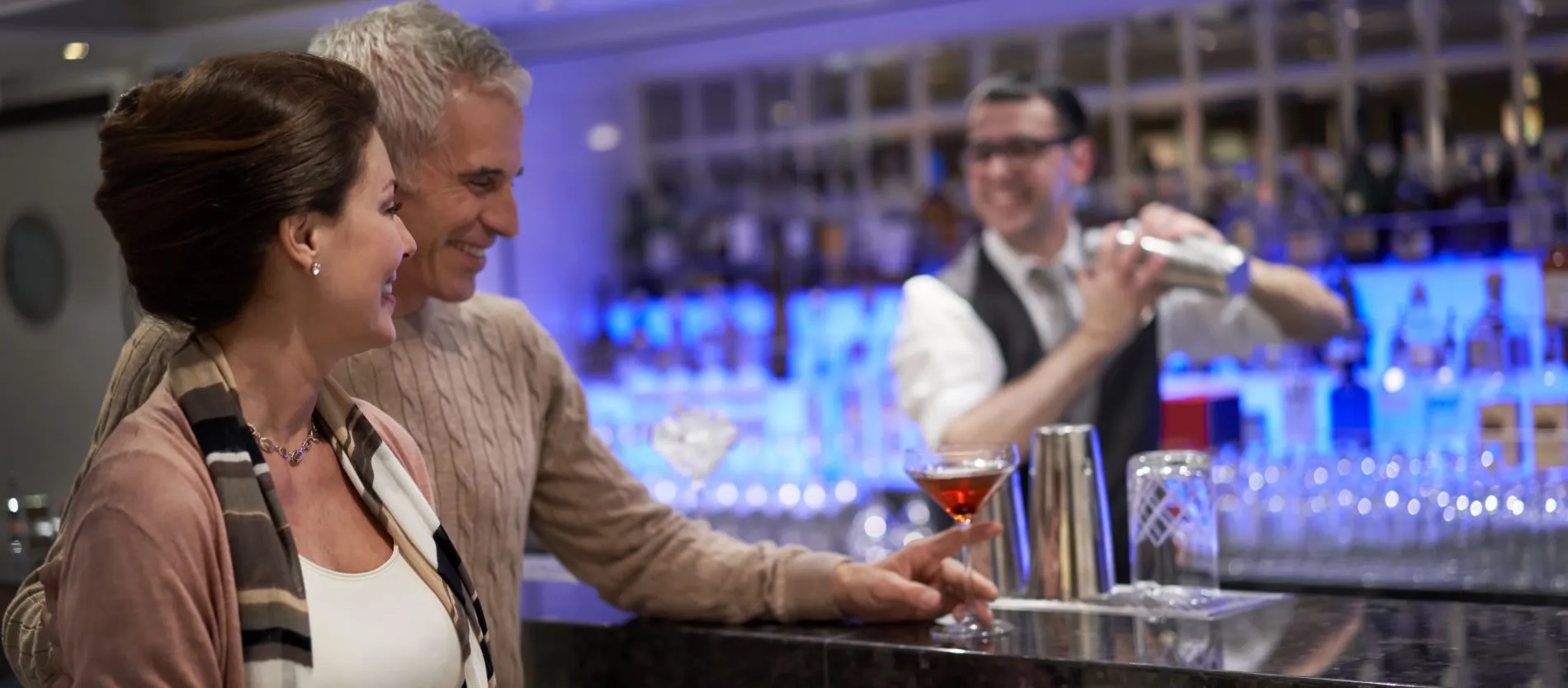 Couple enjoying cocktail at stylish bar with bartender mixing drink