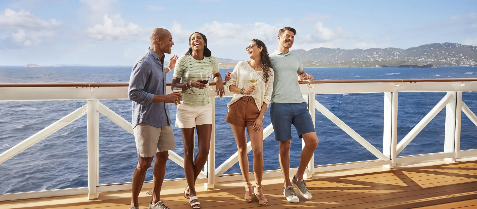 Friends enjoying drinks on a cruise ship deck with ocean and mountains
