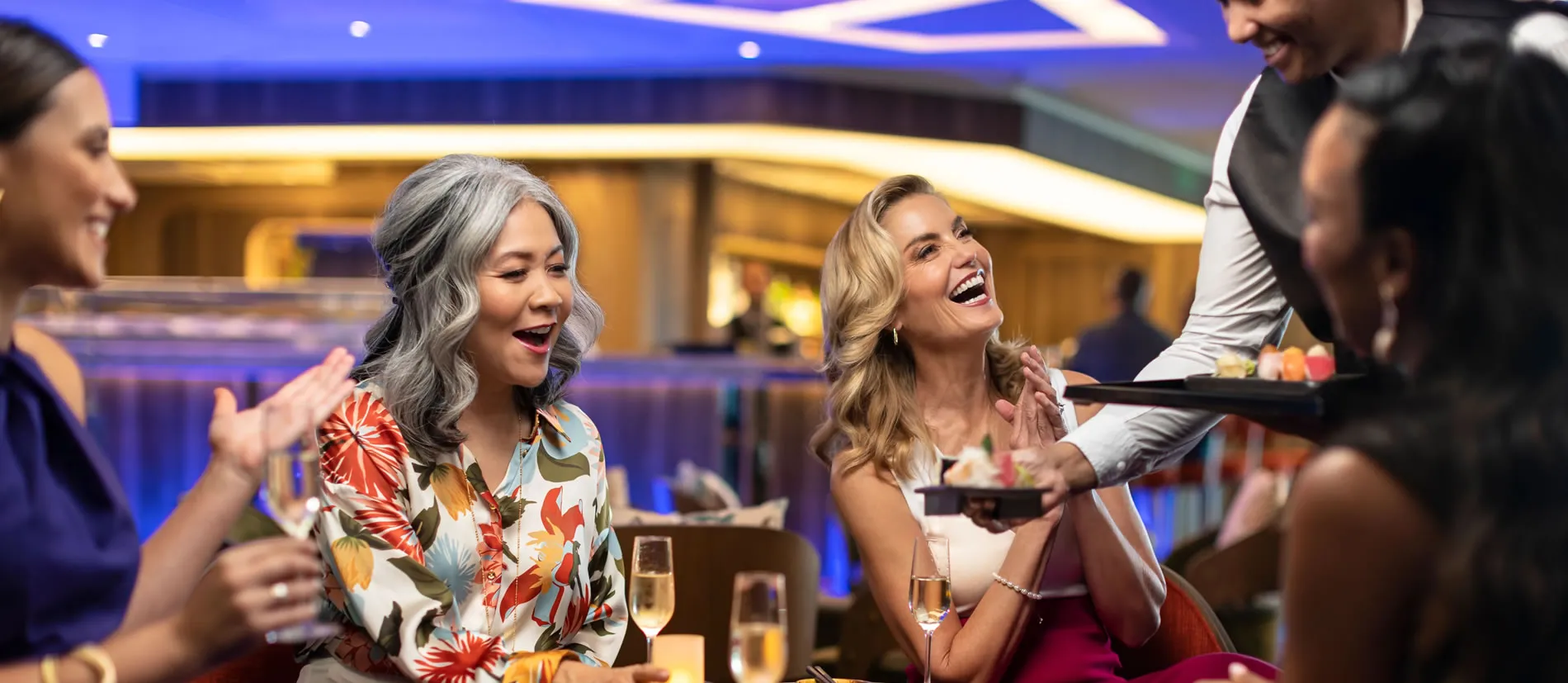 Women laughing together at restaurant with champagne and server nearby