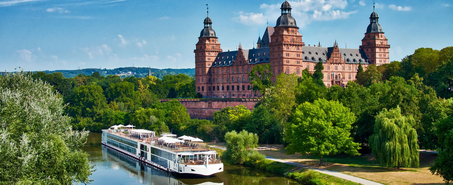 River cruise boat passing historic castle surrounded by lush green landscape