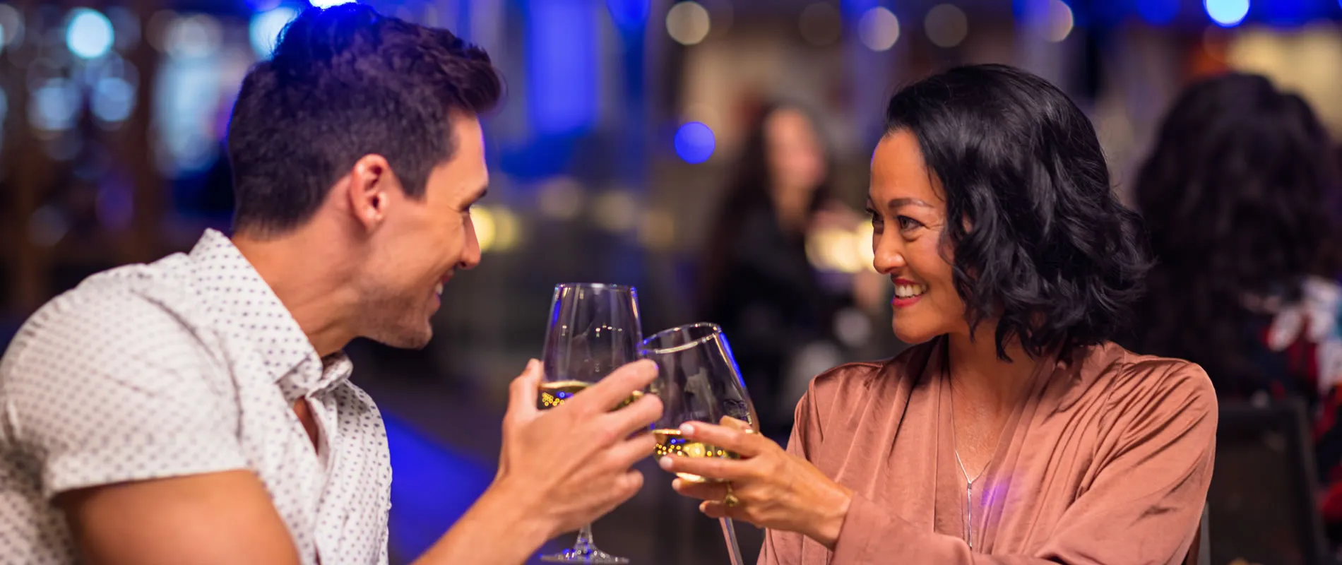 Two people toasting drinks and smiling in a dimly lit bar