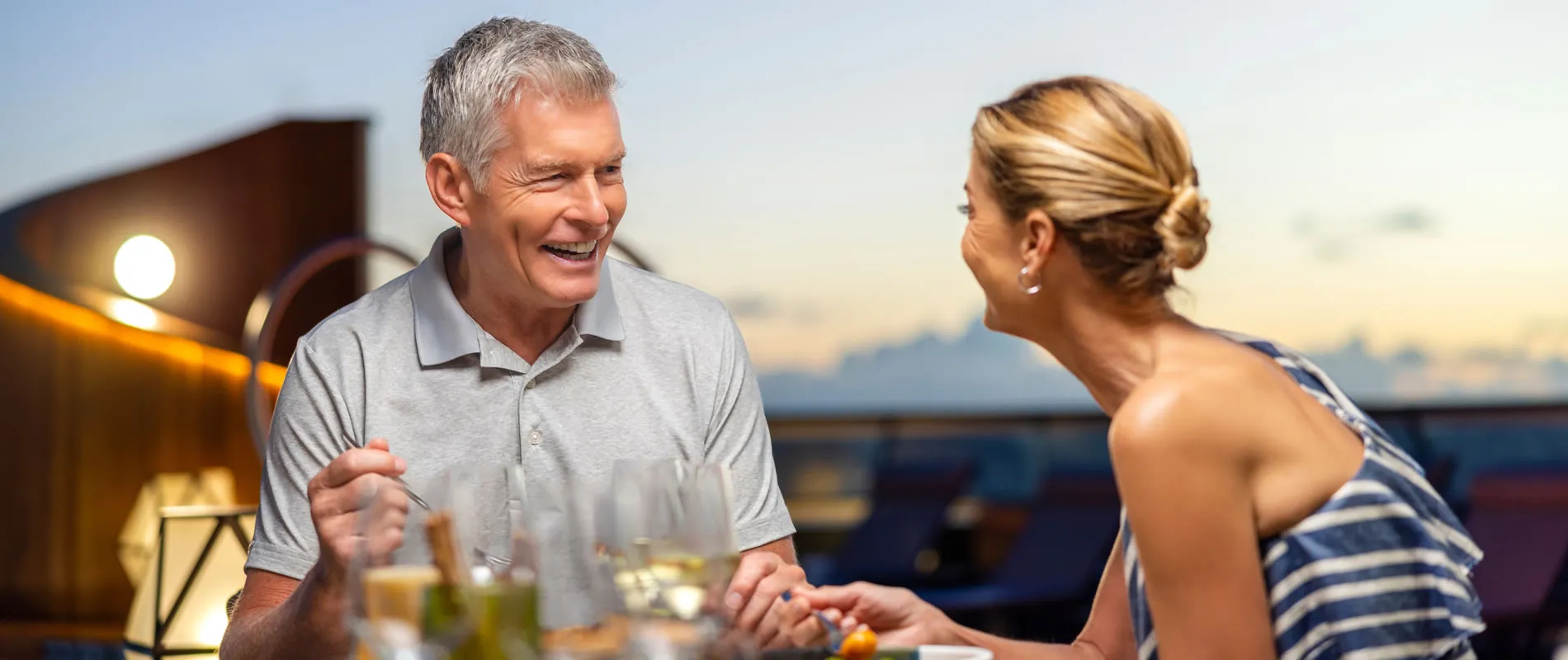 Two people laughing and enjoying drinks together at sunset