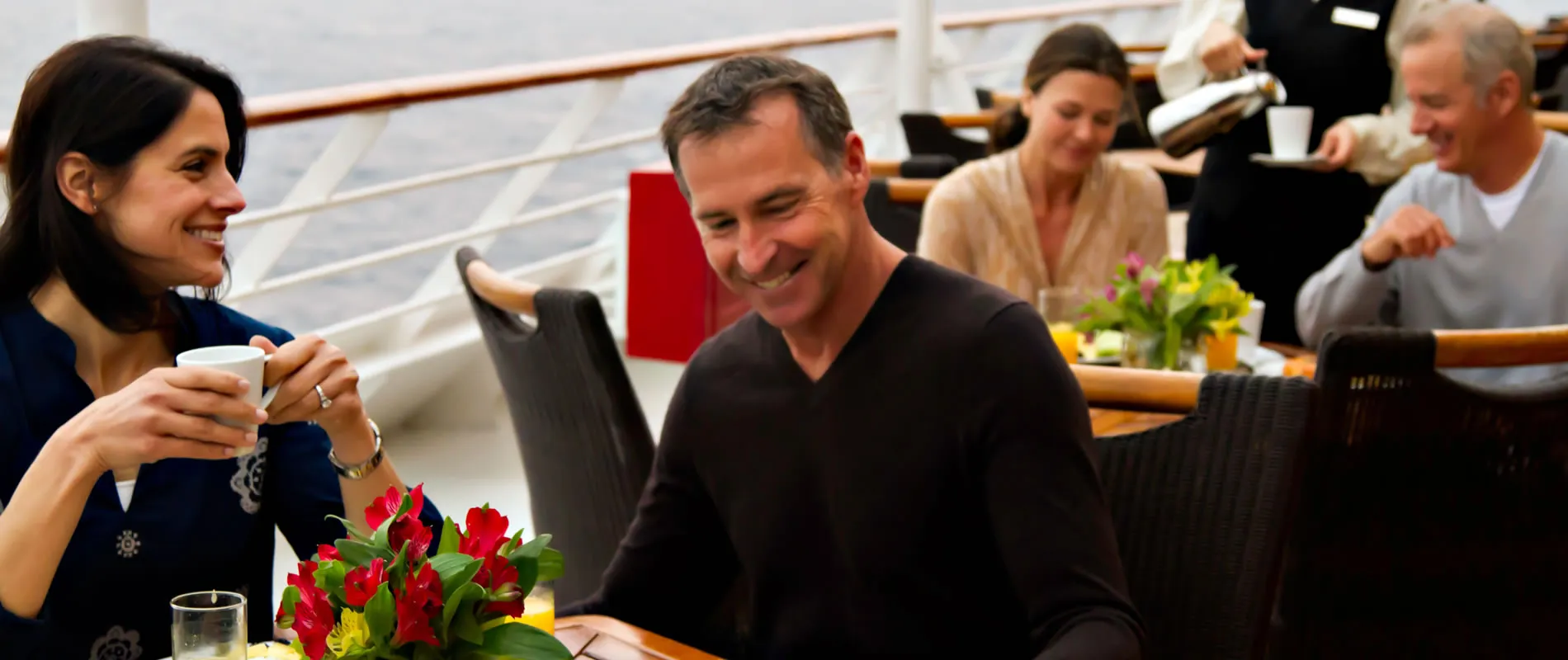 People smiling and enjoying coffee together with red flowers on table