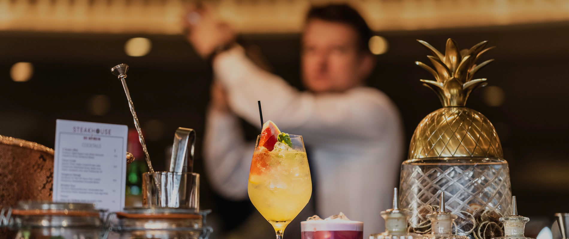 Tropical cocktail with fruit garnish on bar counter with golden pineapple decor