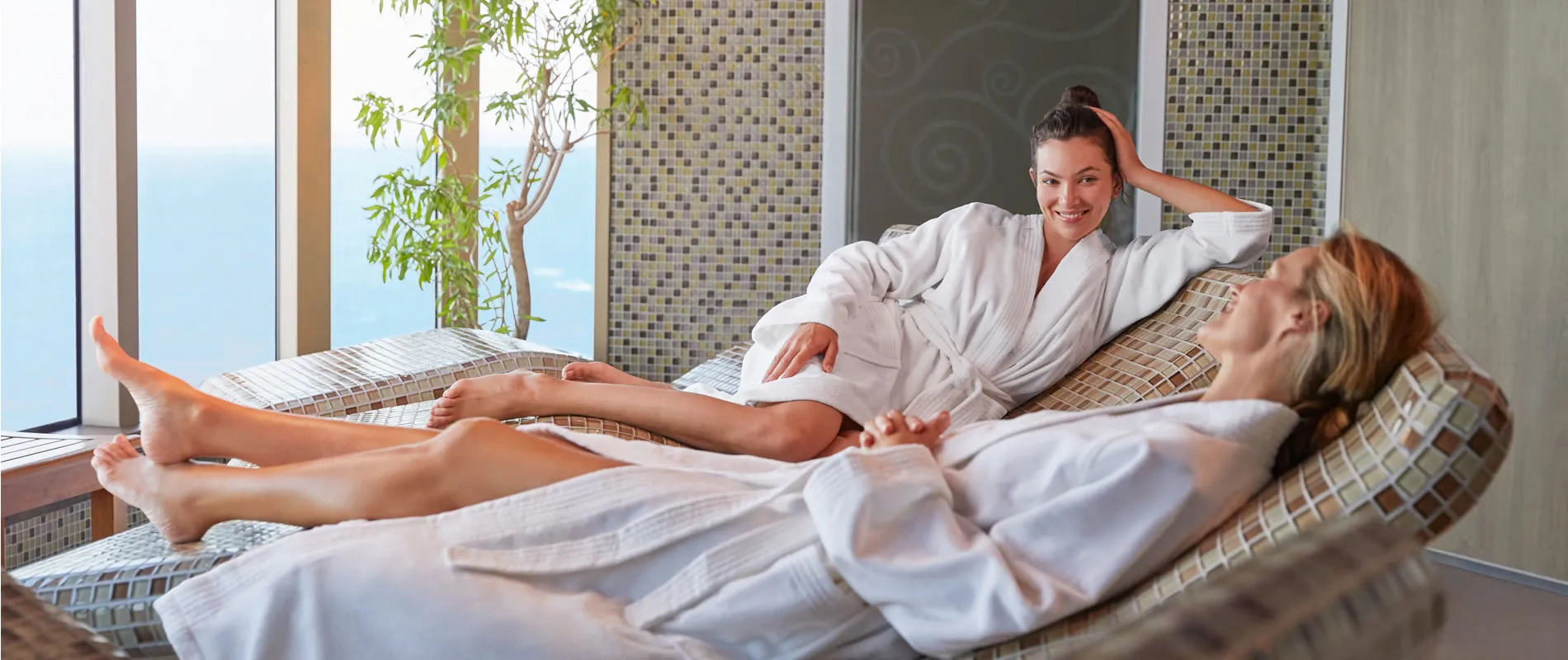 Two women relaxing in white robes at a spa with ocean view
