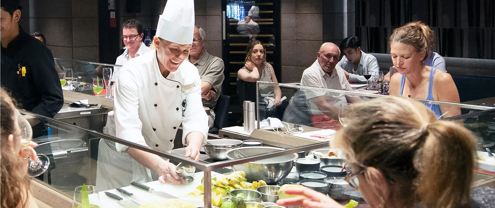 Chef preparing food at open kitchen counter with diners watching