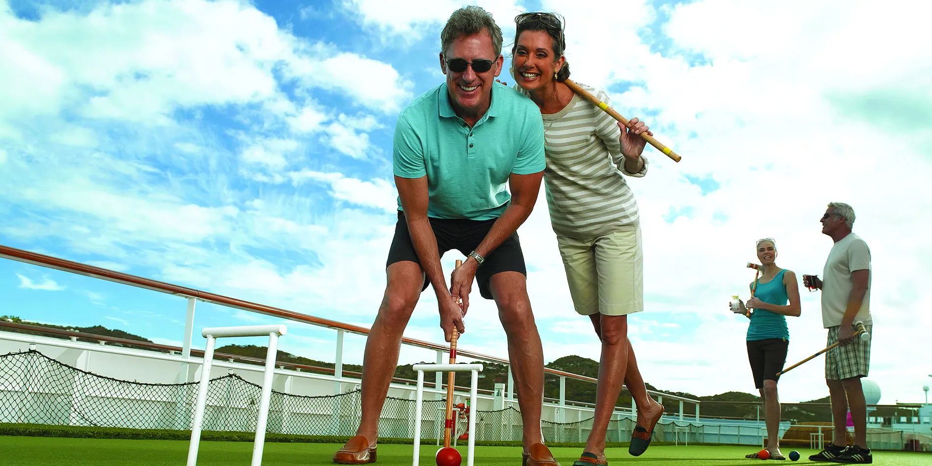 Smiling people playing croquet on a sunny deck with ocean view