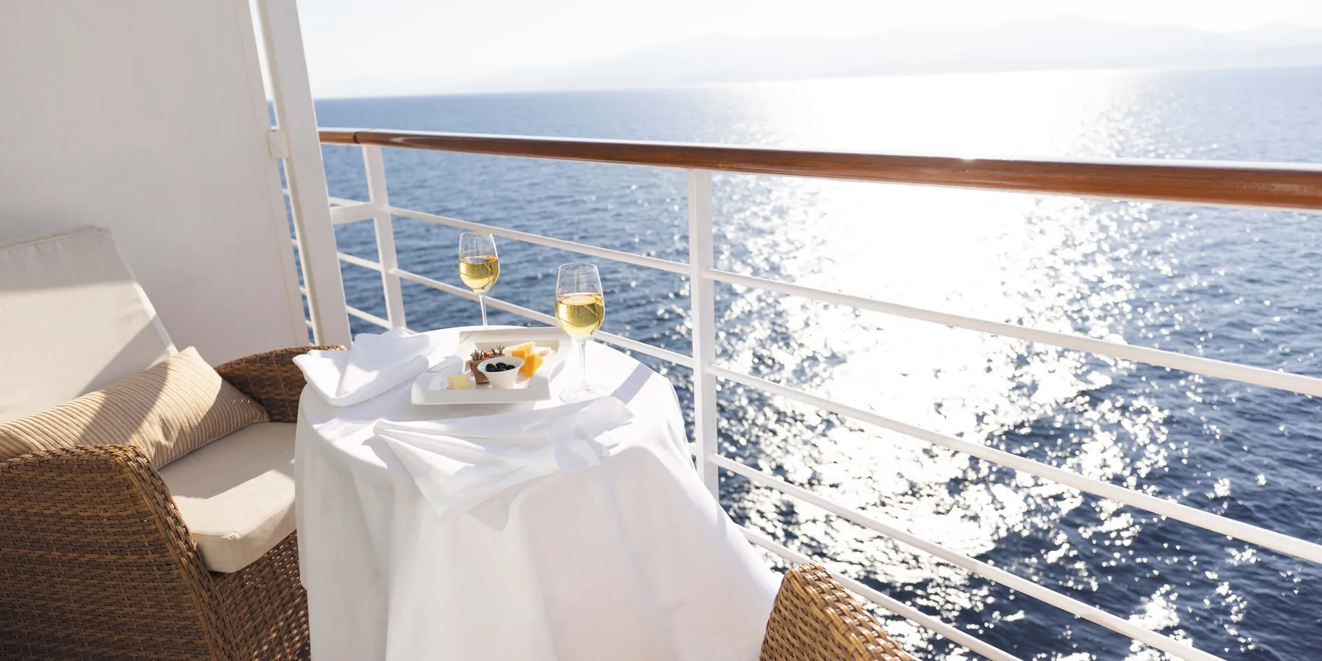 Wine glasses and snacks on cruise ship balcony overlooking sparkling ocean
