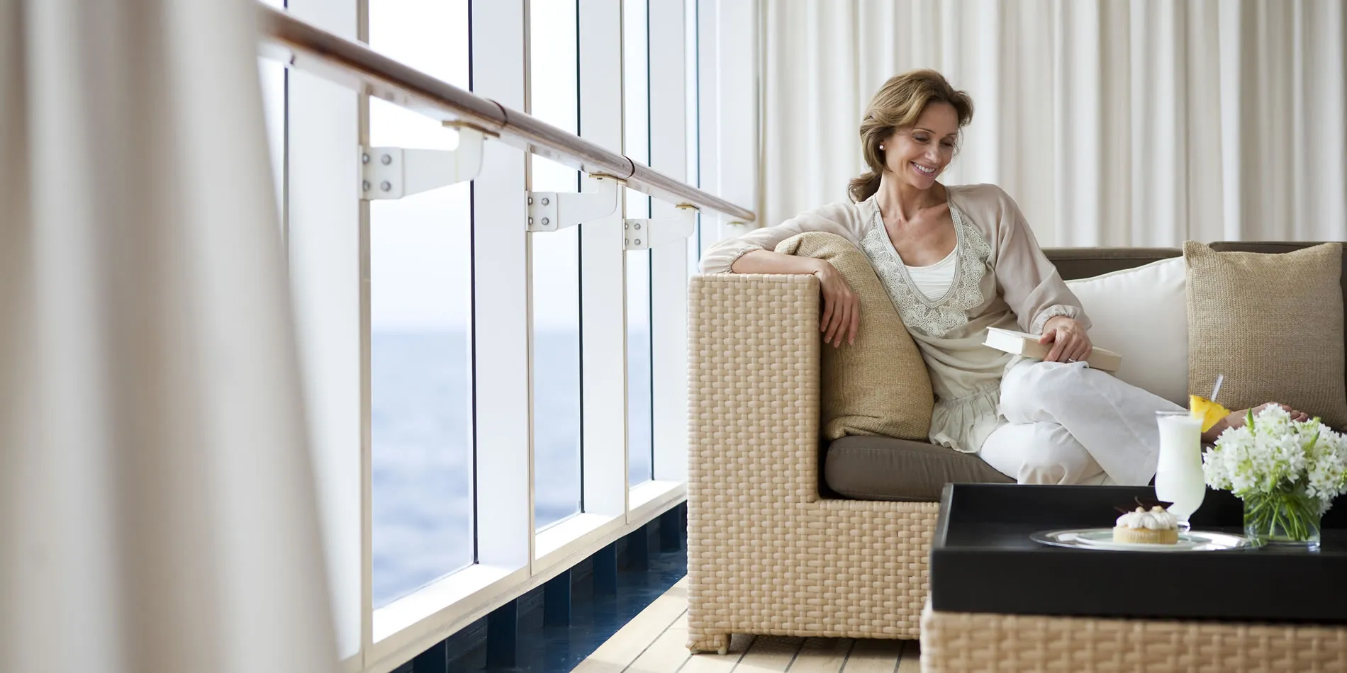 Woman relaxing on woven couch near large window with ocean view