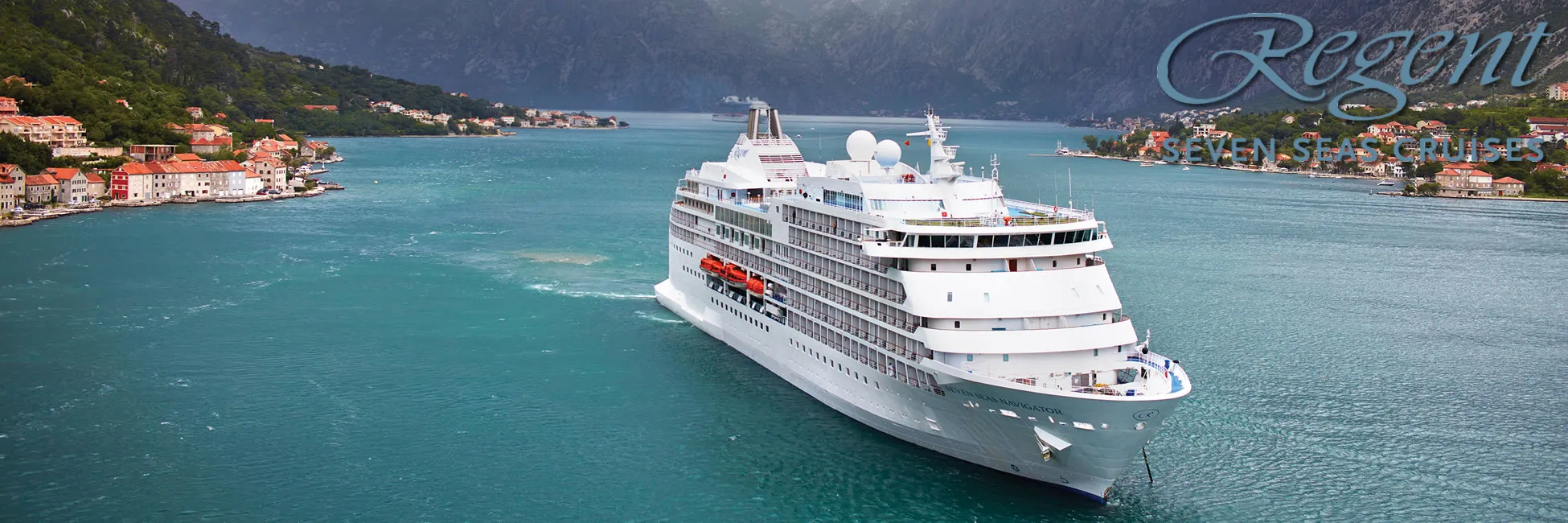 White cruise ship sailing through scenic mountainous coastal town with turquoise waters