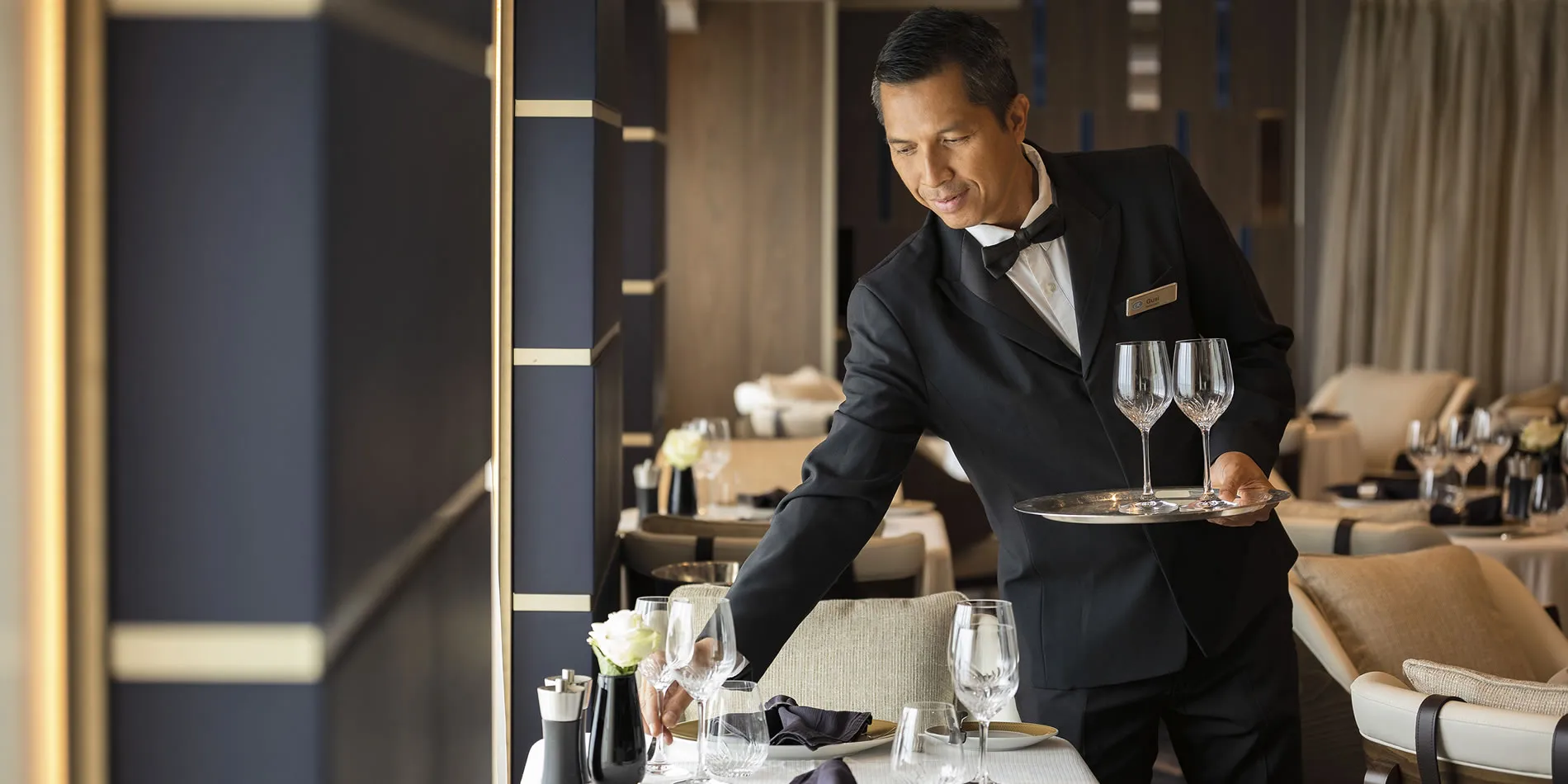 Waiter in tuxedo carefully preparing elegant dining table with wine glasses