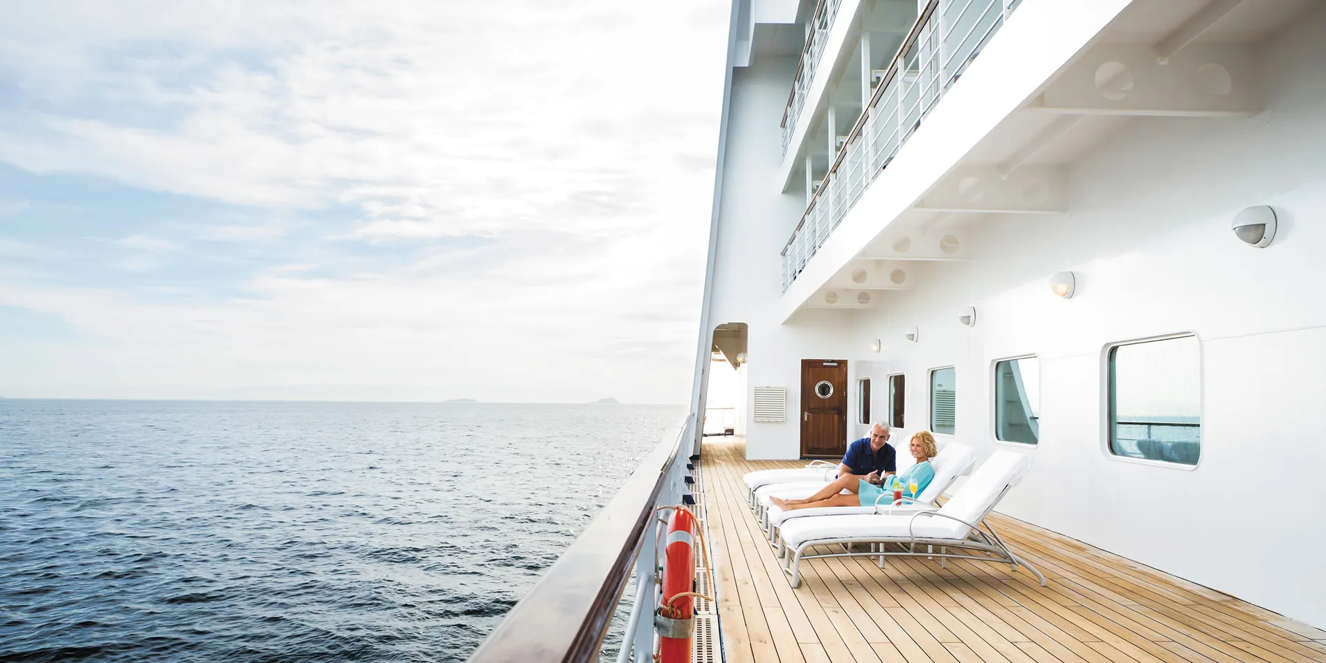 Couple relaxing on cruise ship deck with ocean view and wooden floors