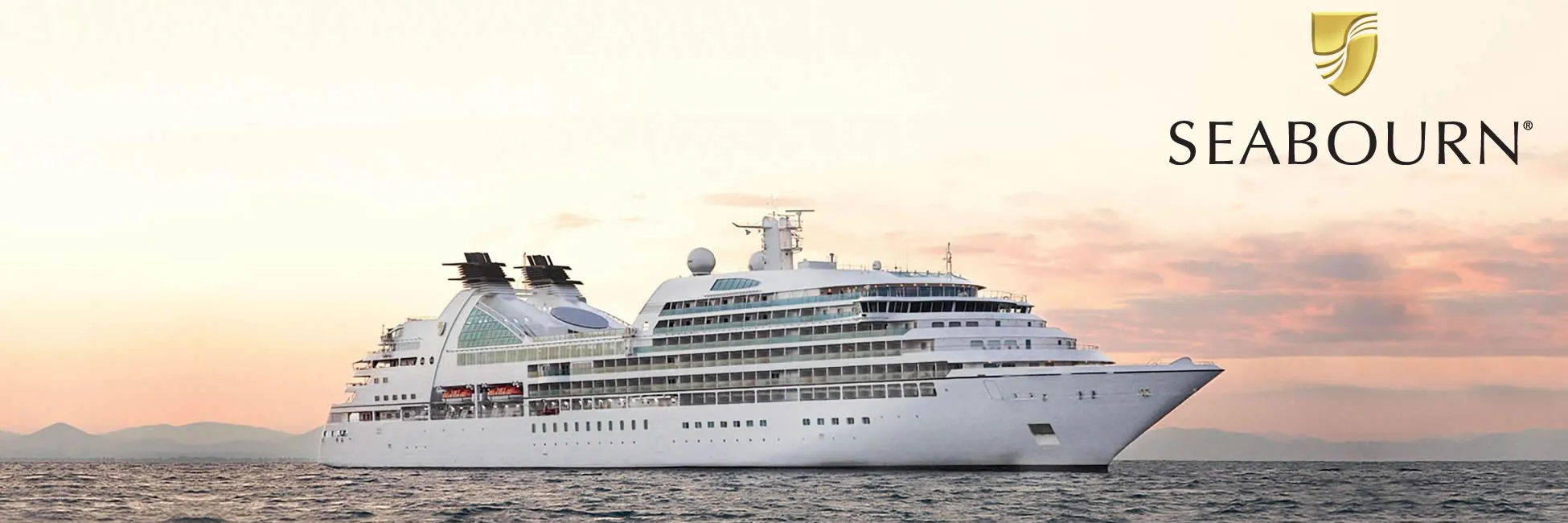 White Seabourn luxury cruise ship sailing at sunset near mountainous coastline
