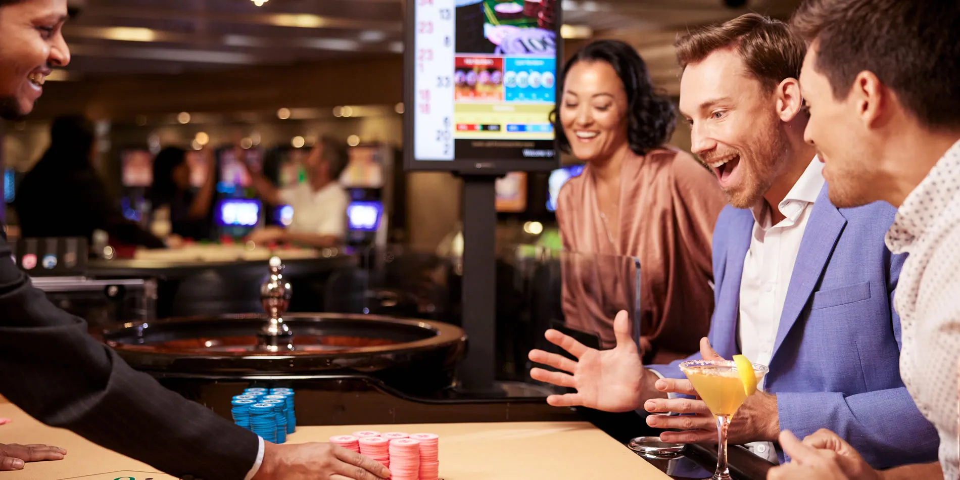 Excited friends playing roulette and enjoying drinks at casino