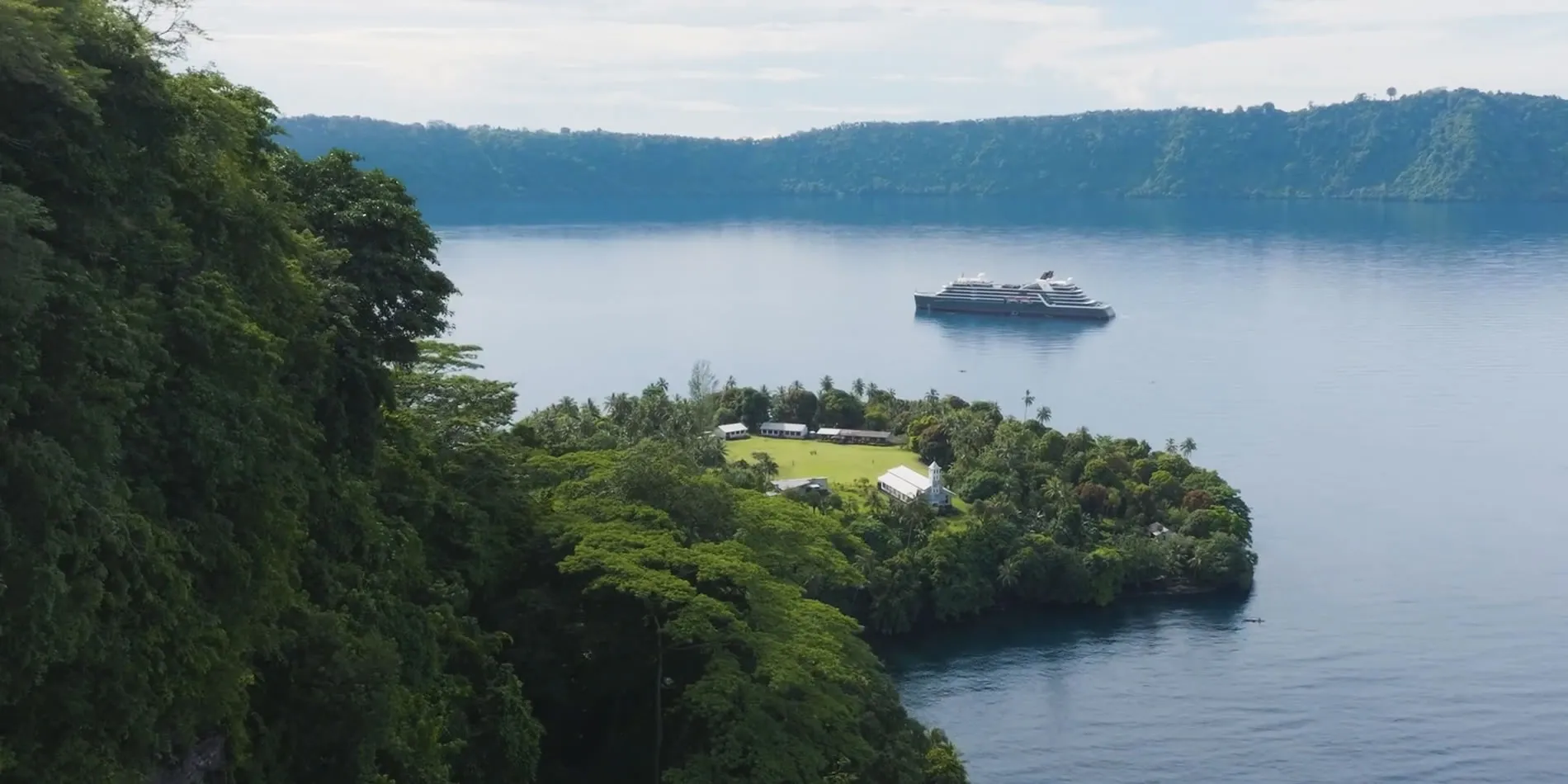 Cruise ship near lush tropical island with buildings surrounded by forest