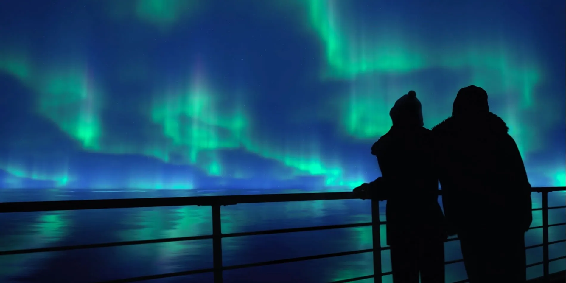 Silhouetted figures watching vibrant green Northern Lights over ocean