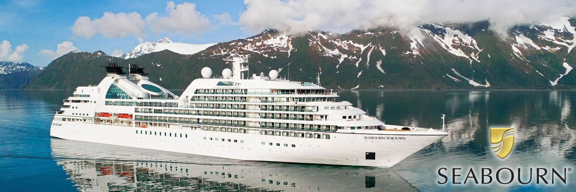 Seabourn cruise ship sailing in Alaskan fjords with snow-capped mountains
