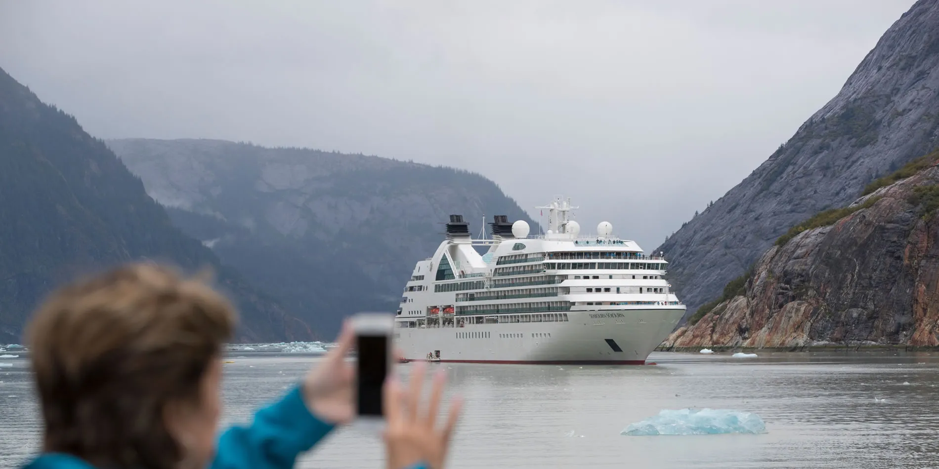 Cruise ship sailing through misty fjord with rocky mountains and small icebergs