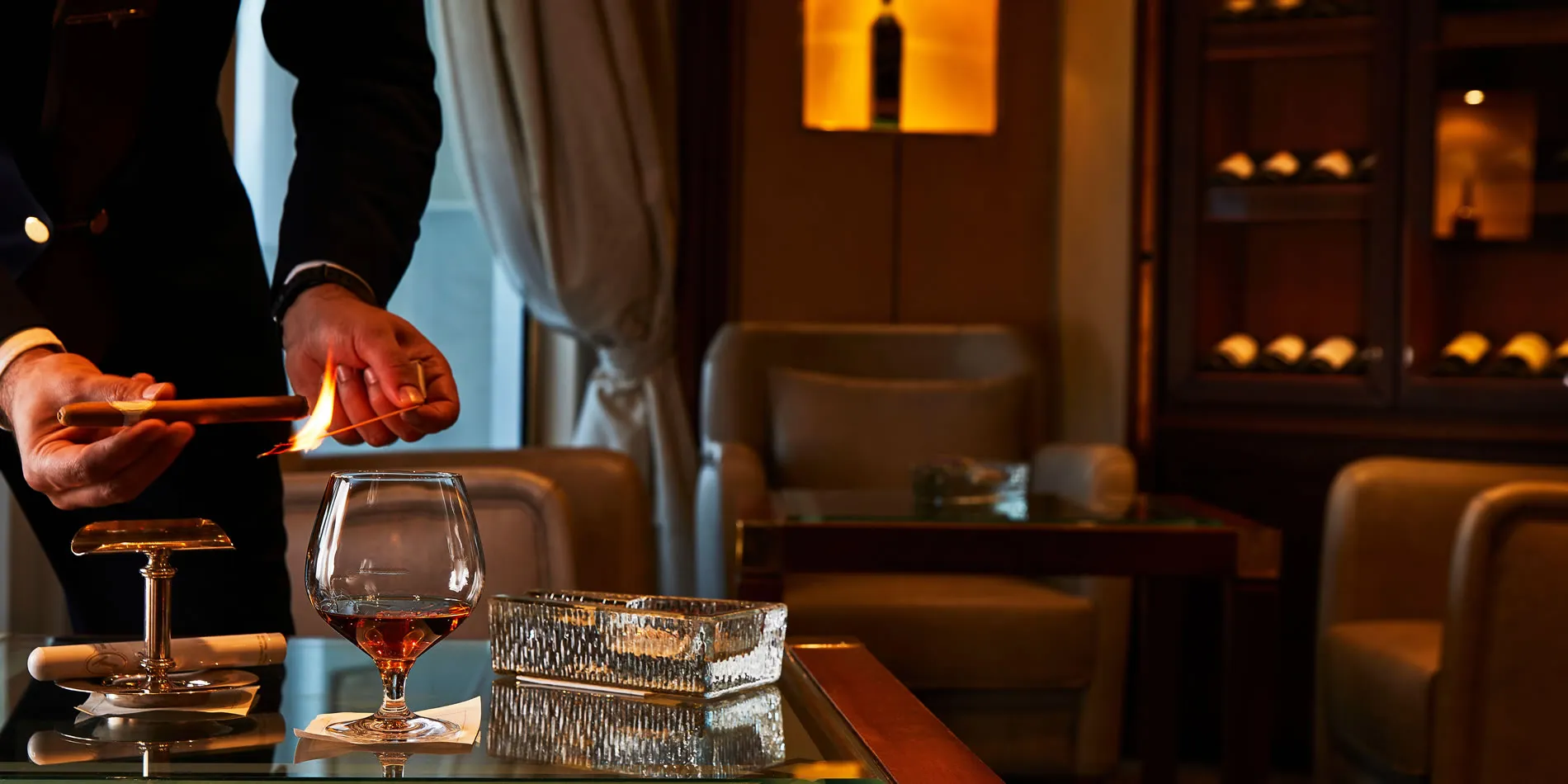 Bartender lighting cigar with cognac glass in elegant lounge setting