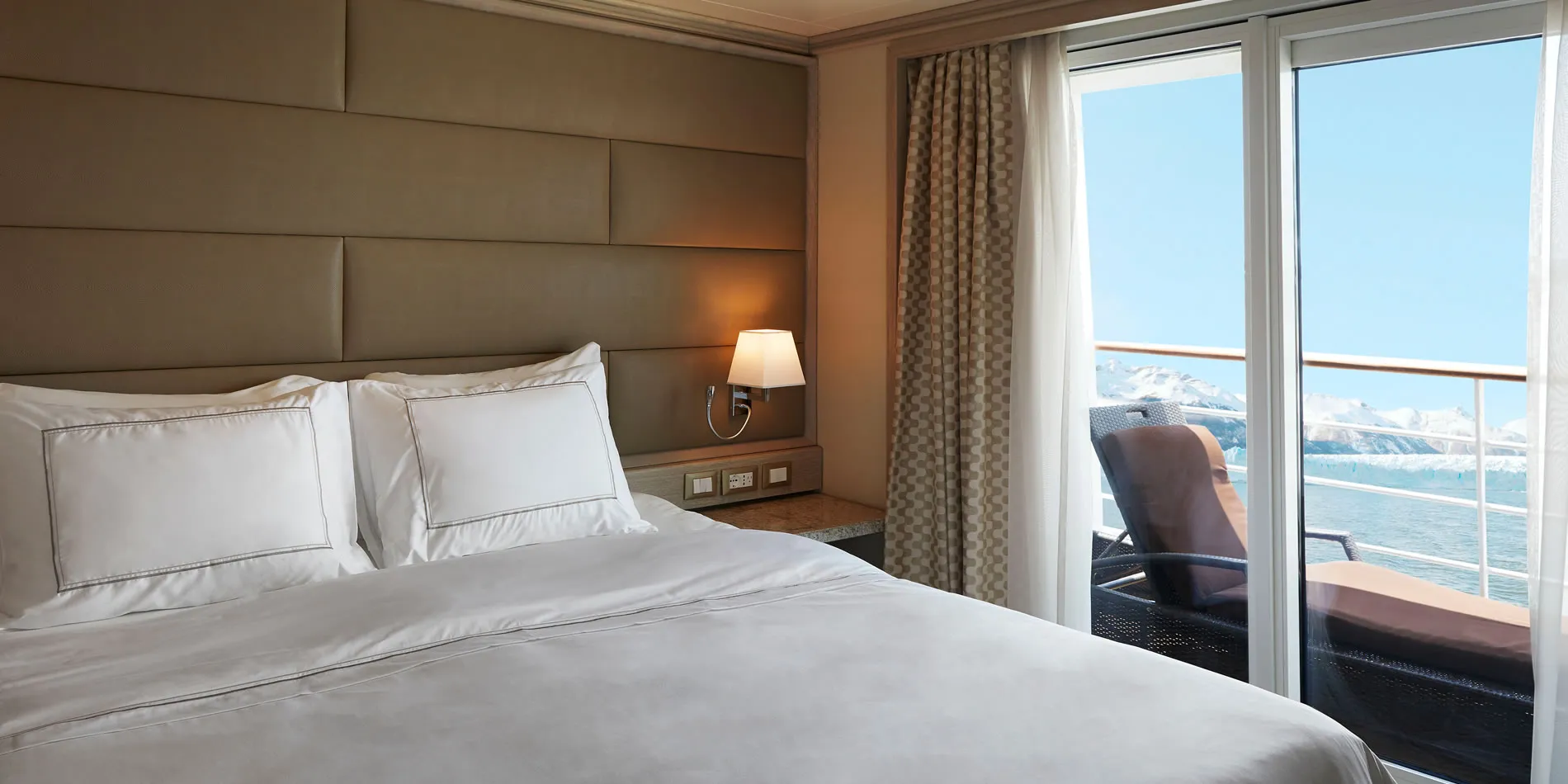 Cruise ship cabin with white bedding and large window overlooking ocean