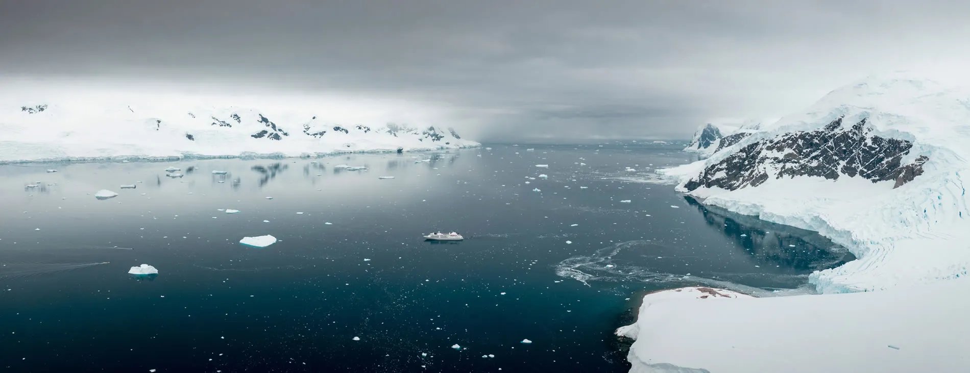 Cruise ship navigating through icy Antarctic waters with snow-covered mountains