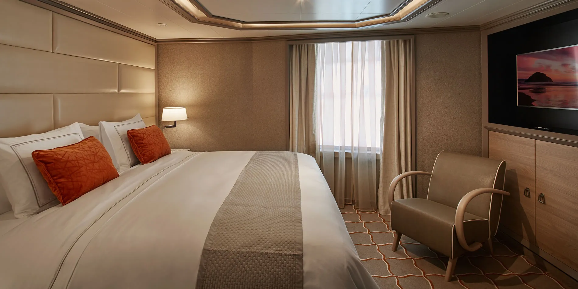 Luxurious hotel room with white bed, orange pillows, and ocean sunset artwork