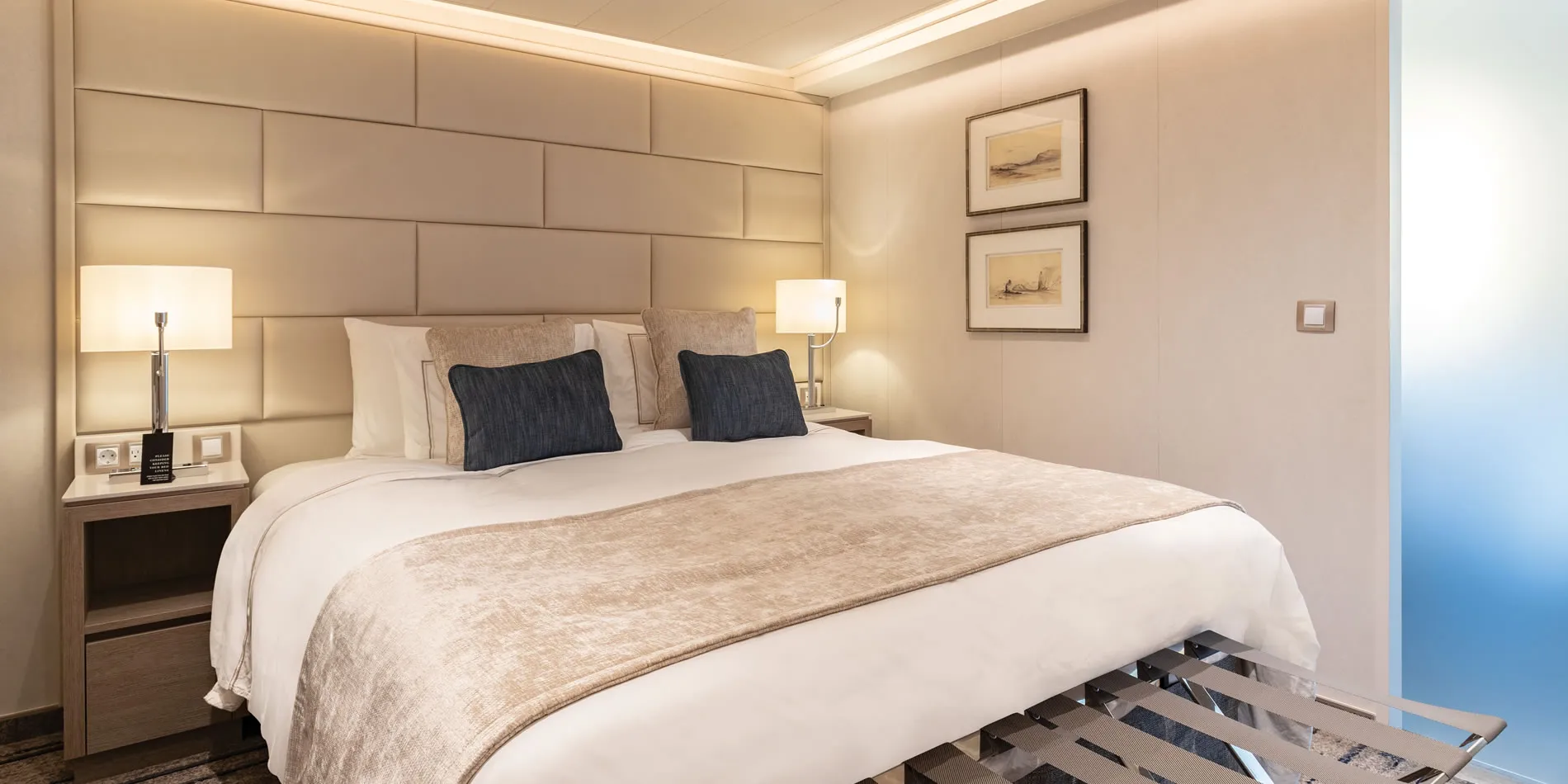 Elegant hotel bedroom with padded wall, white bed, and nautical artwork