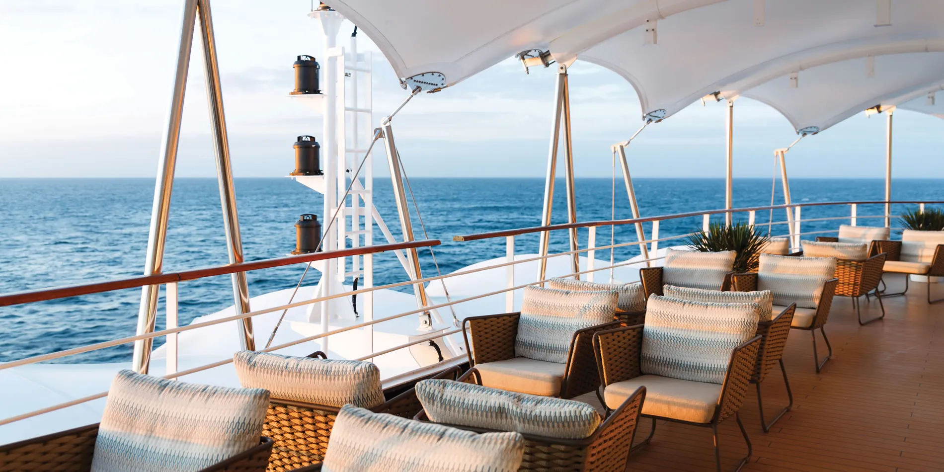 Outdoor deck of cruise ship with woven chairs overlooking blue ocean