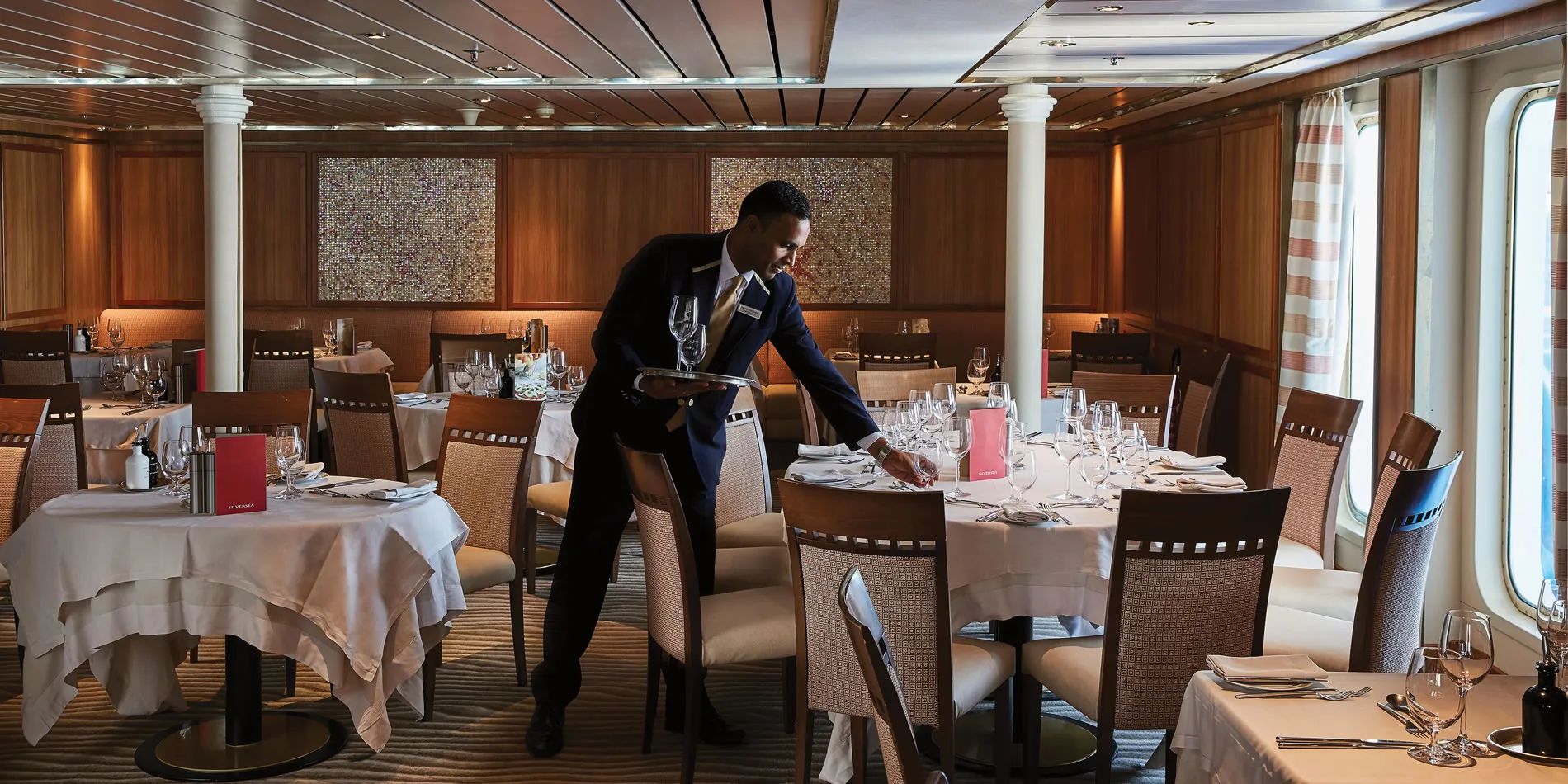 Waiter preparing dining tables in elegant cruise ship restaurant