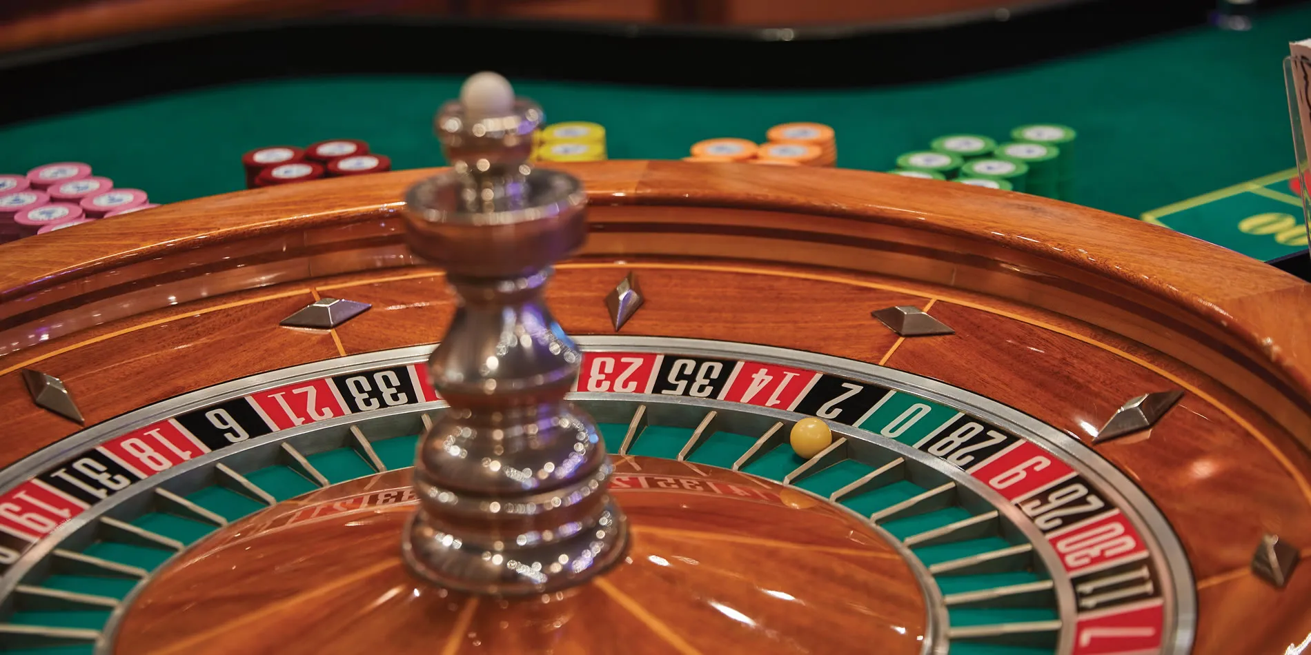 Wooden roulette wheel with colorful casino chips on green table