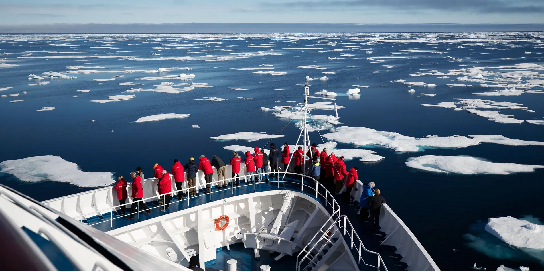 Expedition ship navigating through icy Arctic waters with tourists in red jackets