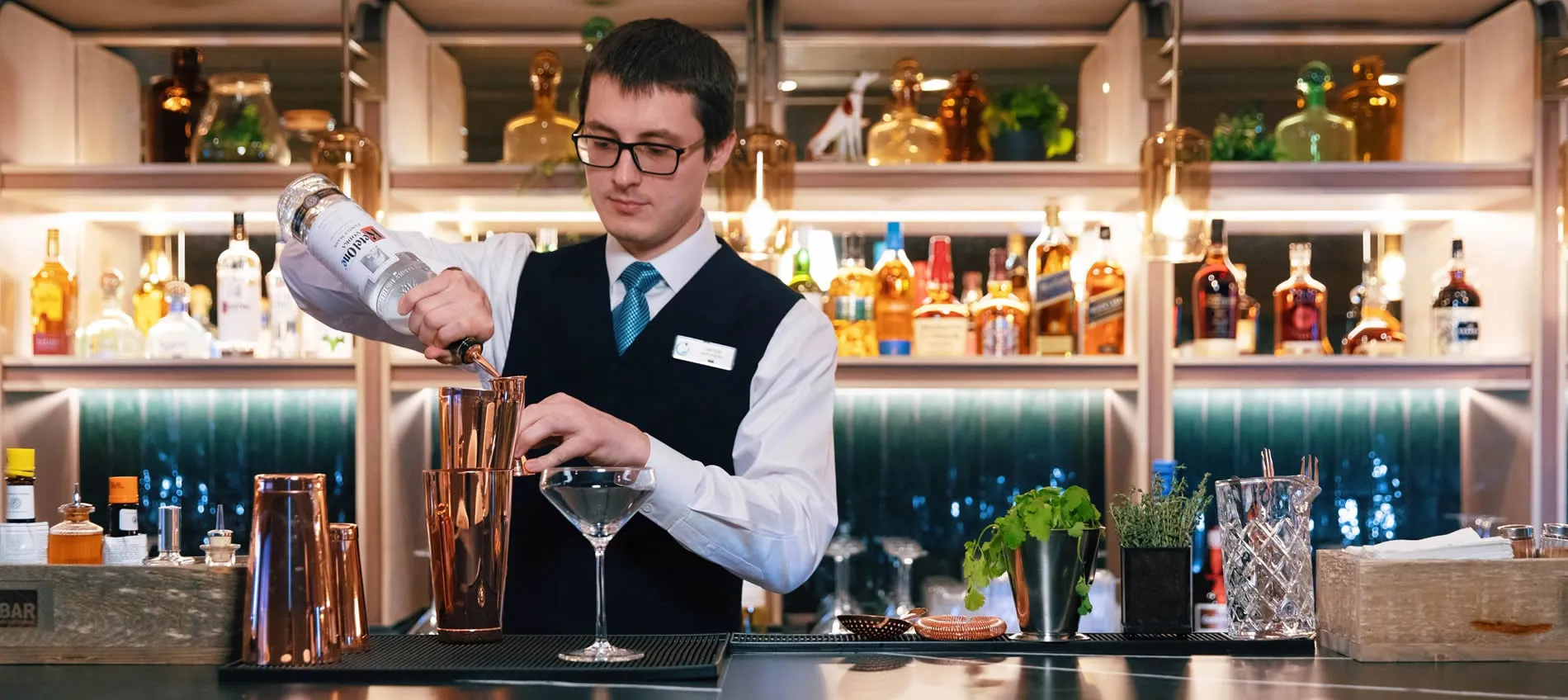 Professional bartender pouring cocktail behind bar with various liquor bottles