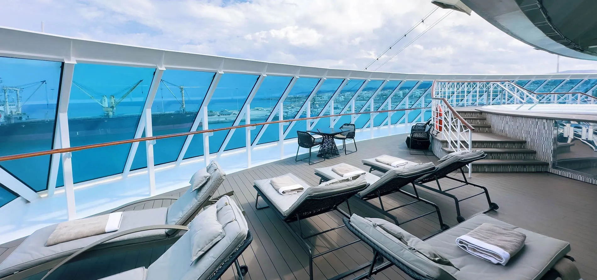 Cruise ship deck with lounge chairs overlooking ocean and port