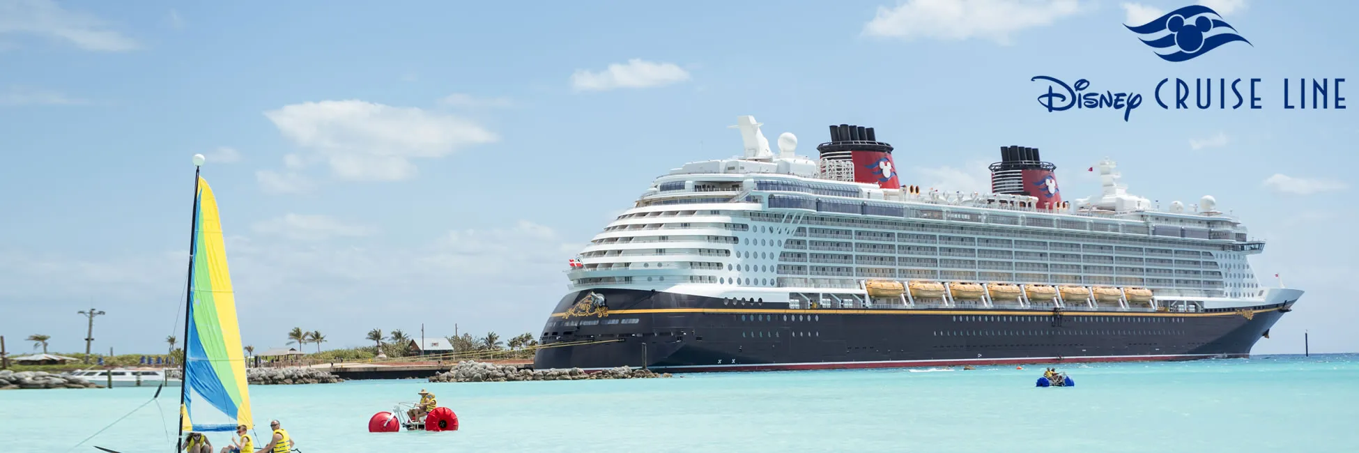 Disney Cruise Line ship docked at tropical beach with sailboat and water activities