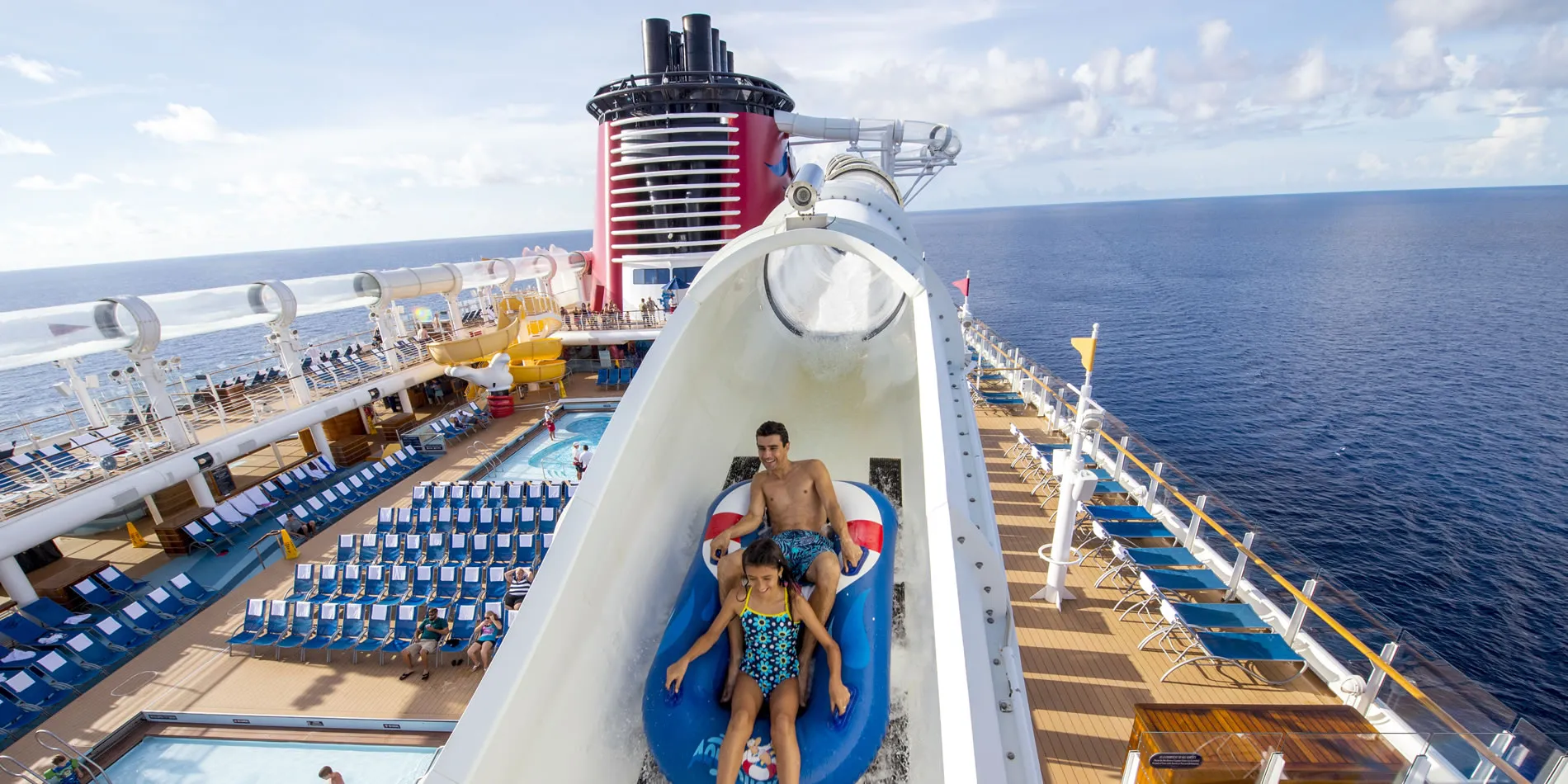 Parent and child sliding down water slide on cruise ship deck