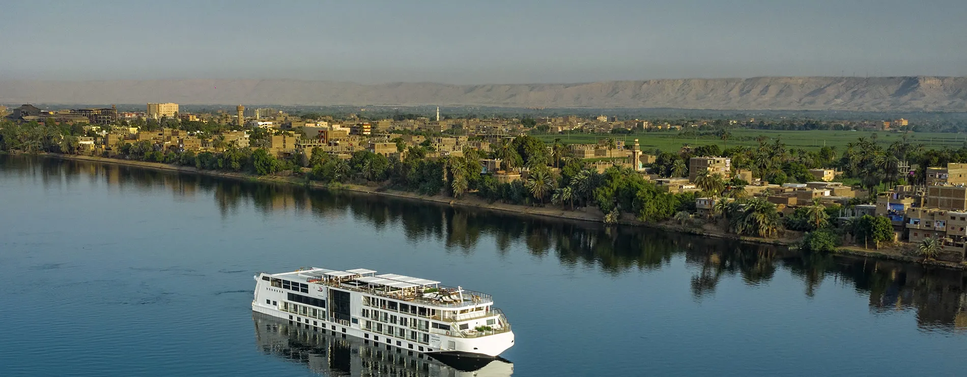 Cruise ship on Nile River with Egyptian city and mountains in background