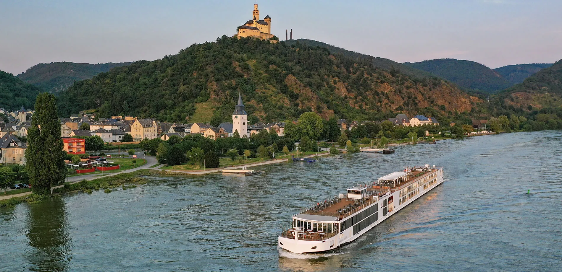 River cruise ship passing picturesque castle and village along scenic riverbank