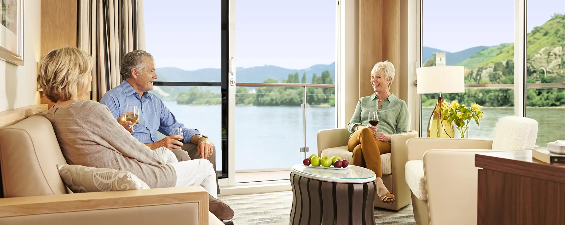 Seniors relaxing with wine in elegant room overlooking scenic river and mountains