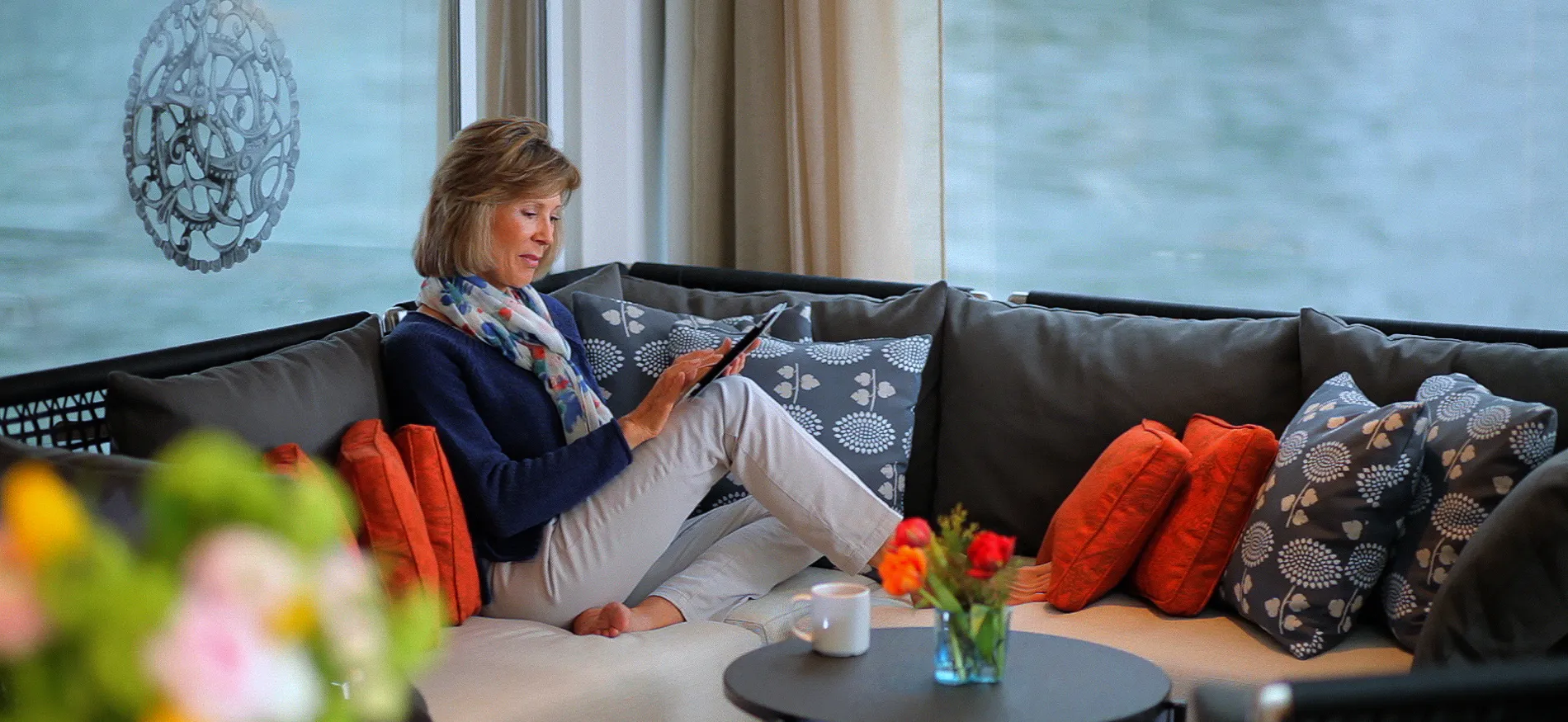 Woman relaxing on couch, reading tablet with coffee and flowers nearby