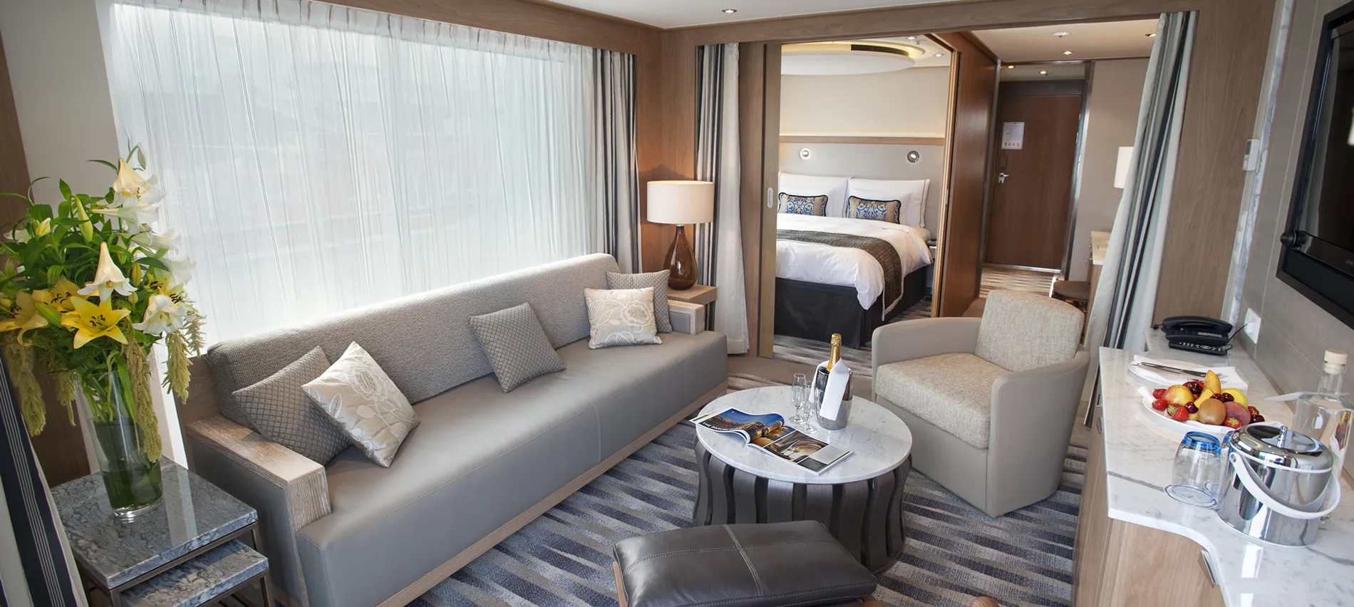 Luxury cruise ship suite with living area, bedroom, and amenities