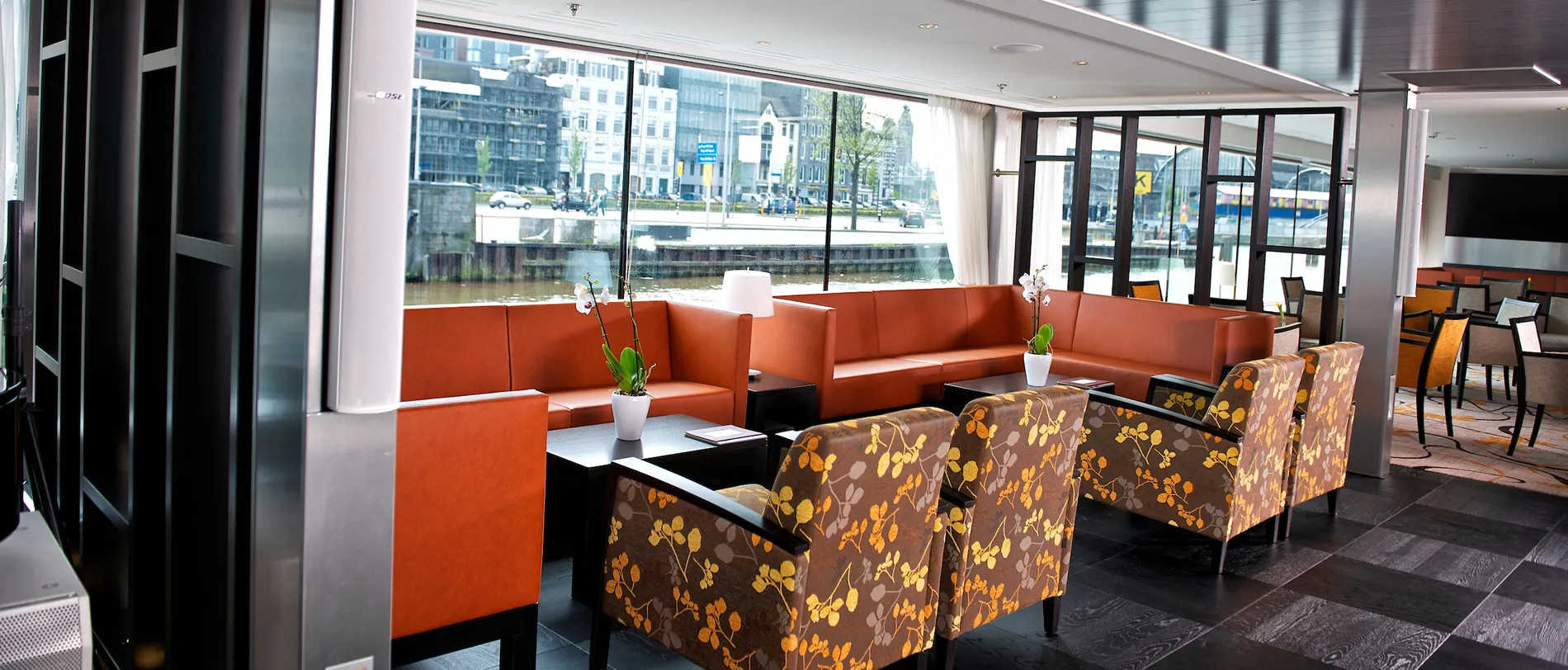Modern lounge with orange seating and large windows overlooking urban waterfront